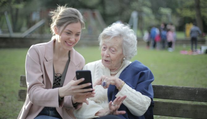 Egy fiatal nő és egy idős nő nézett egy telefonra a padon